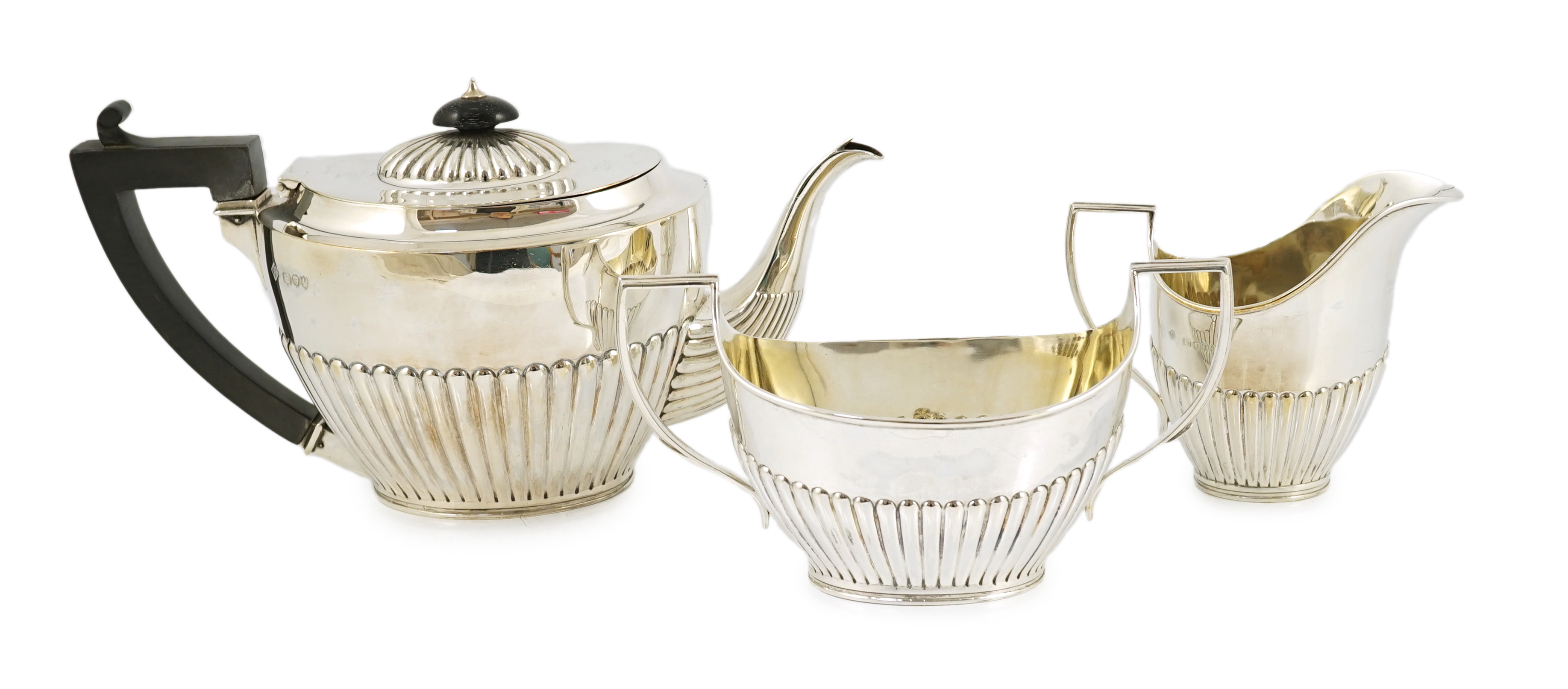 A late Victorian oak cased demi-fluted oval silver three piece tea set, by Martin, Hall & Co
